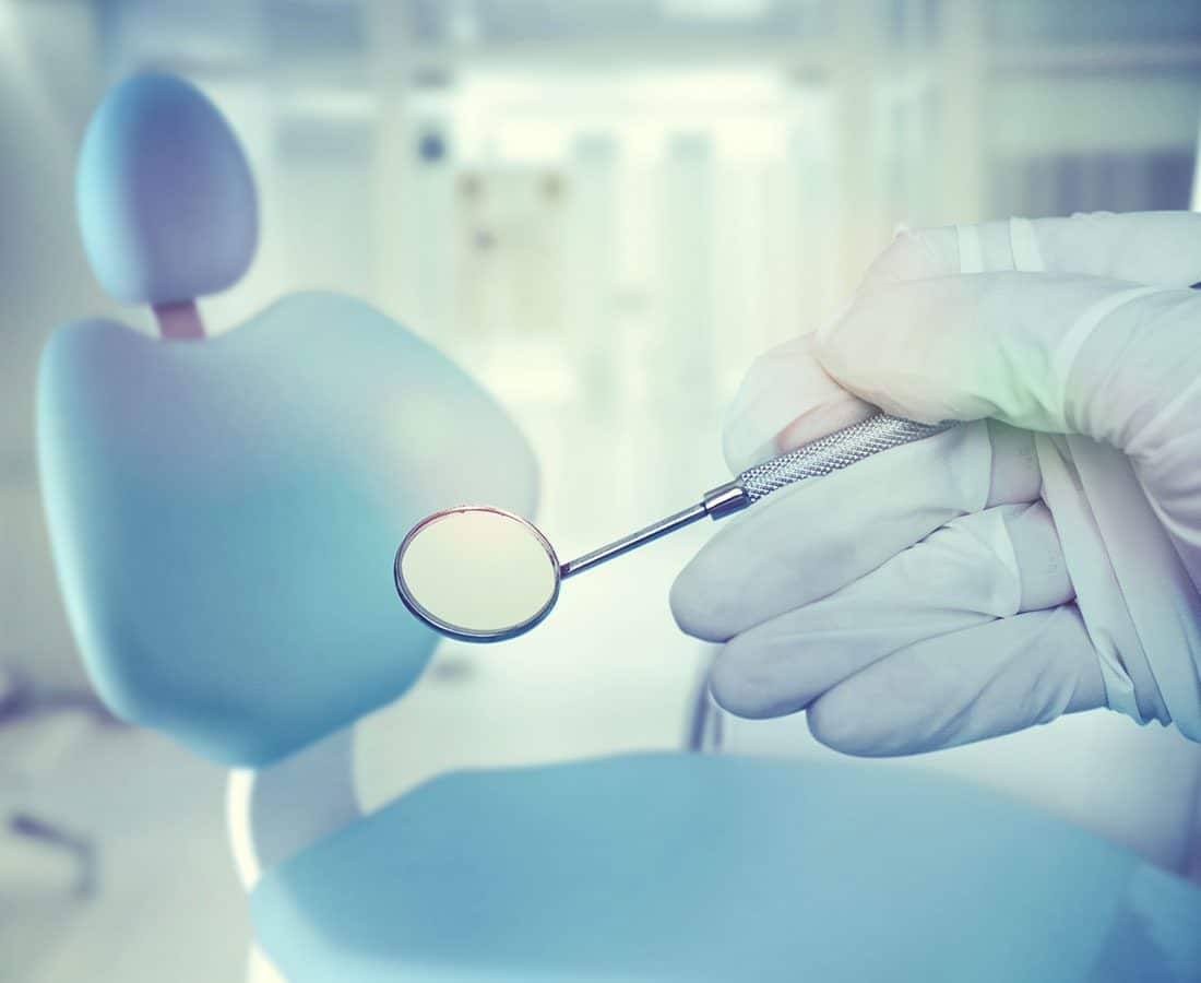 Gloved hand holding dental mirror with dental chair in the background
